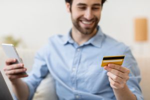 Happy man with smartphone and credit card shopping online