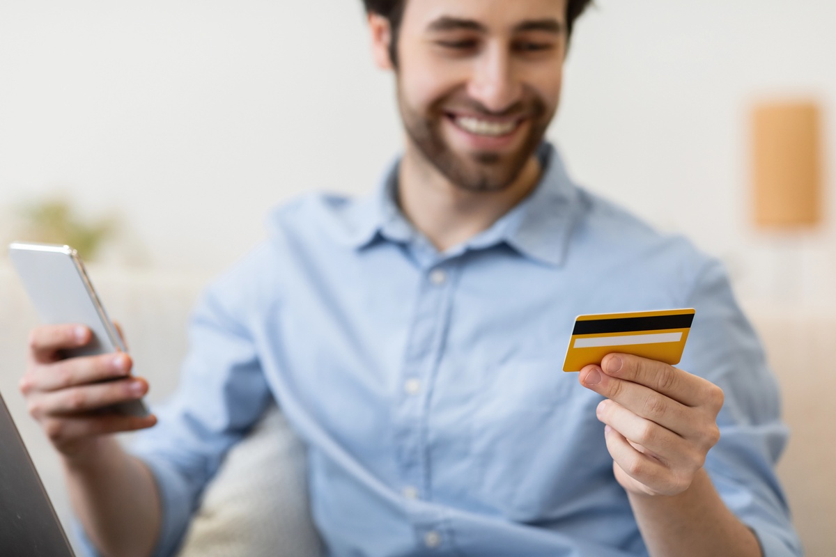 Happy man with smartphone and credit card shopping online