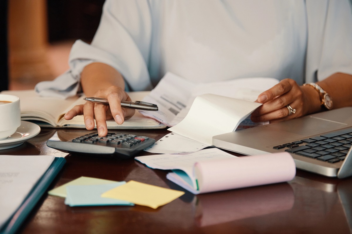 woman on a calculator at a desk, surrounded by a laptop and papers, focused on work and figures