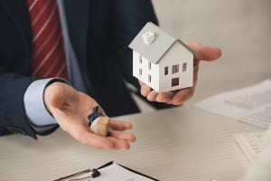 man dressed in a suit presents a house model, indicating a business or real estate theme
