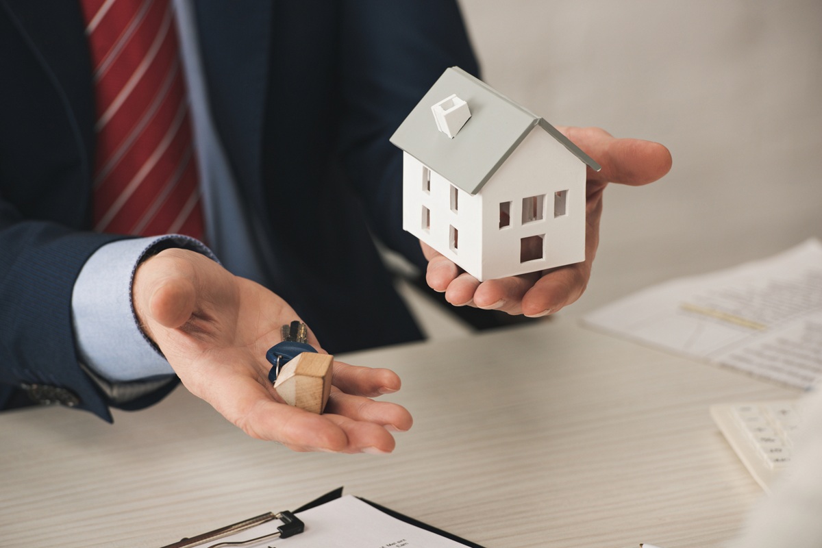 man dressed in a suit presents a house model, indicating a business or real estate theme